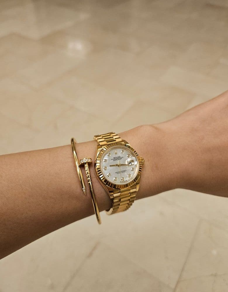 Layering jewelry with a Rolex gold Datejust with ten diamond markers.